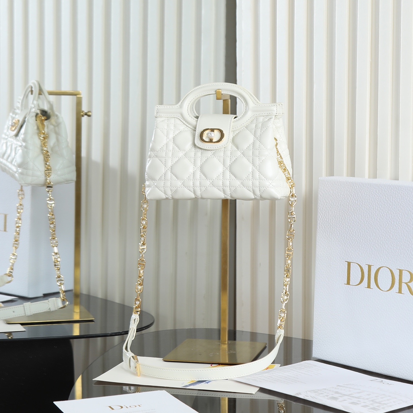 原廠級 白色鏈條手袋
這款 Dior Jolie Top Handle 迷你鏈條手袋是二零二六早春成衣系列新品，呈現出優雅精緻的設計。採用黑色羊皮革精心製作，飾以藤格紋，翻蓋點綴以金色飾面金屬 CD 標誌和白色樹脂珠飾。內設一個隔層，可收納各種日常用品。搭配雙頂部手柄和可調節、可拆卸 CD 鏈條肩帶，肩帶由皮革帶和 CD 鏈環組成，飾以白色樹脂珠飾，可舒適手提、肩背或斜挎，可與日常或晚裝造型搭配。
