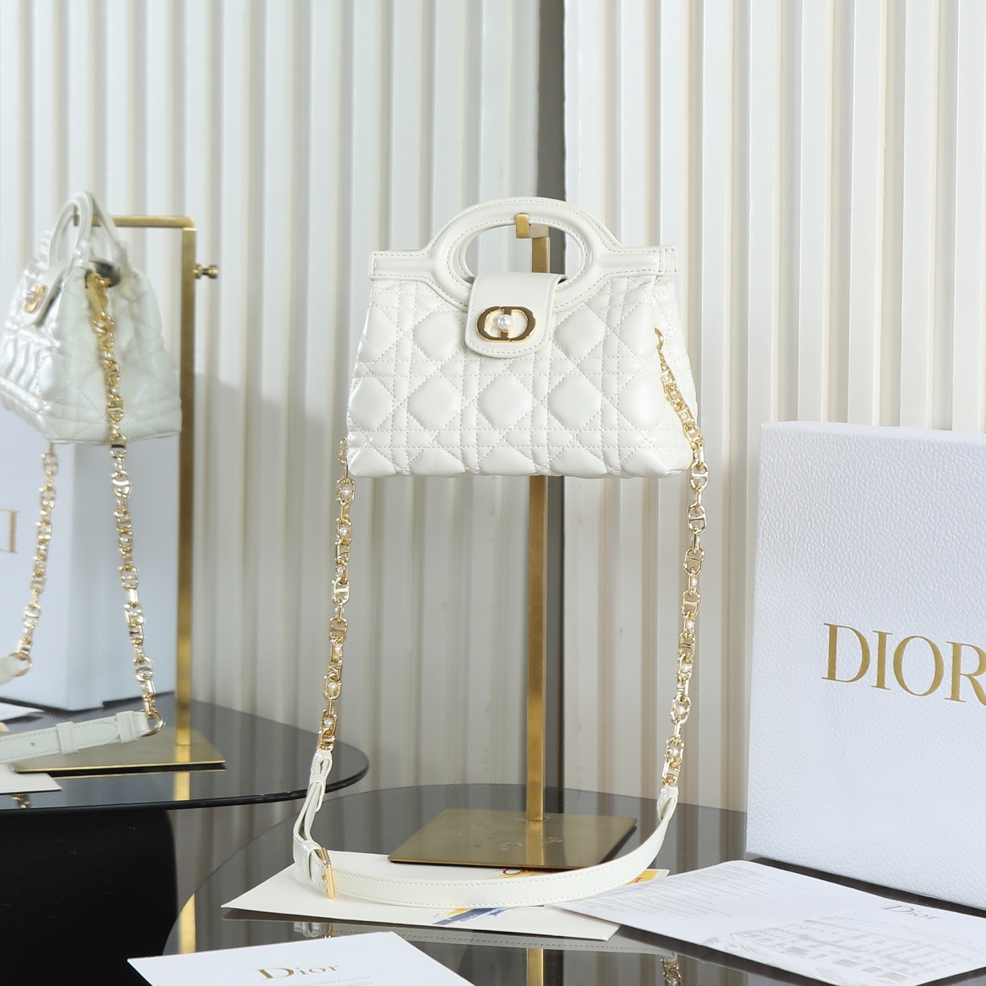 原廠級 白色鏈條手袋
這款 Dior Jolie Top Handle 迷你鏈條手袋是二零二六早春成衣系列新品，呈現出優雅精緻的設計。採用黑色羊皮革精心製作，飾以藤格紋，翻蓋點綴以金色飾面金屬 CD 標誌和白色樹脂珠飾。內設一個隔層，可收納各種日常用品。搭配雙頂部手柄和可調節、可拆卸 CD 鏈條肩帶，肩帶由皮革帶和 CD 鏈環組成，飾以白色樹脂珠飾，可舒適手提、肩背或斜挎，可與日常或晚裝造型搭配。
