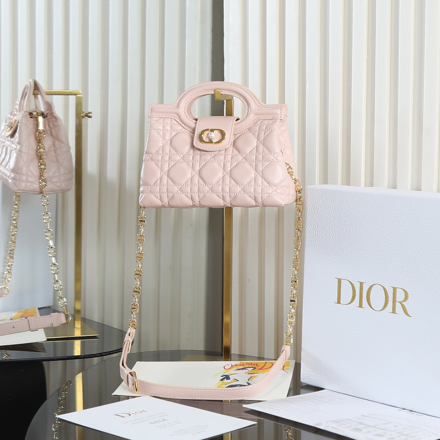 原廠級 粉色鏈條手袋
這款 Dior Jolie Top Handle 迷你鏈條手袋是二零二六早春成衣系列新品，呈現出優雅精緻的設計。採用黑色羊皮革精心製作，飾以藤格紋，翻蓋點綴以金色飾面金屬 CD 標誌和白色樹脂珠飾。內設一個隔層，可收納各種日常用品。搭配雙頂部手柄和可調節、可拆卸 CD 鏈條肩帶，肩帶由皮革帶和 CD 鏈環組成，飾以白色樹脂珠飾，可舒適手提、肩背或斜挎，可與日常或晚裝造型搭配。
