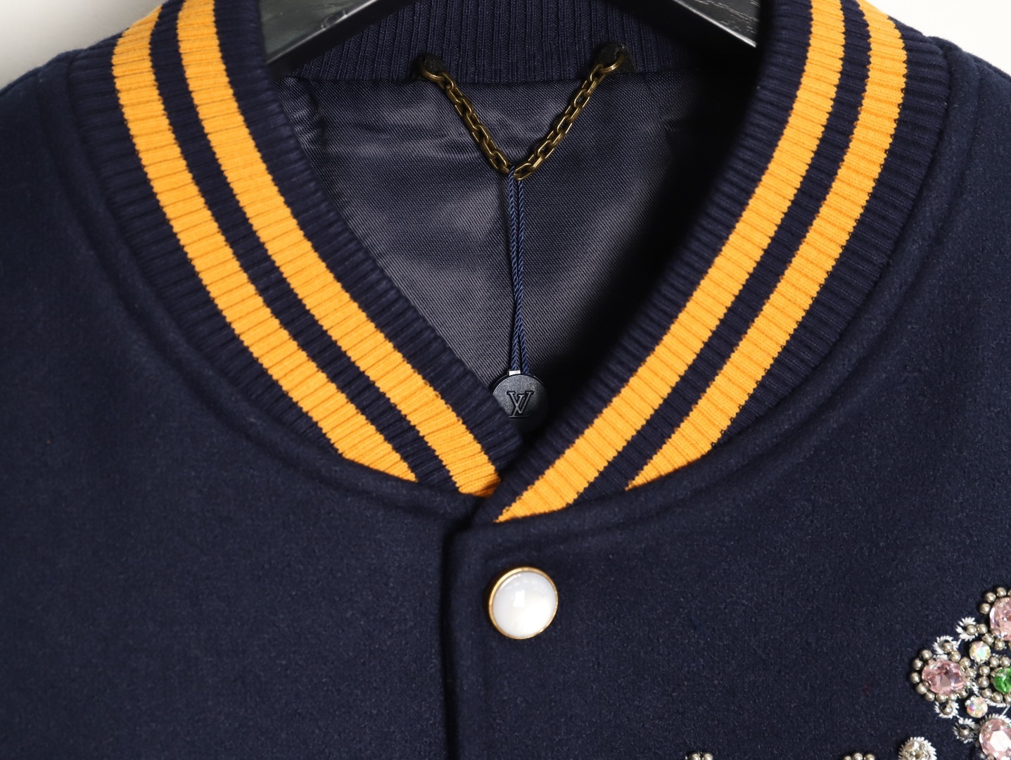 Louis Vuitton/路易威登 26ss 水鑽刺繡棒球服外套
材質拼接：衣身採用藏青色羊毛混紡面料，質感挺括耐磨；袖子為淺棕牛皮材質，柔軟細膩，經典拼皮設計還原美式棒球服復古感。

• 裝飾亮點：左胸位置有重工水鑽+金屬刺繡裝飾，鑲嵌多色寶石與閃鑽，綴有“L.V.M.”字母標識，華麗精緻，辨識度拉滿。

• 版型結構：立領+羅紋條紋領口/袖口/下擺，防風且修飾身形；正面按扣開合，兩側配有插袋，兼顧實用與美觀。
球帽點綴，休閒隨性又有街頭感。
N Size:S-XL