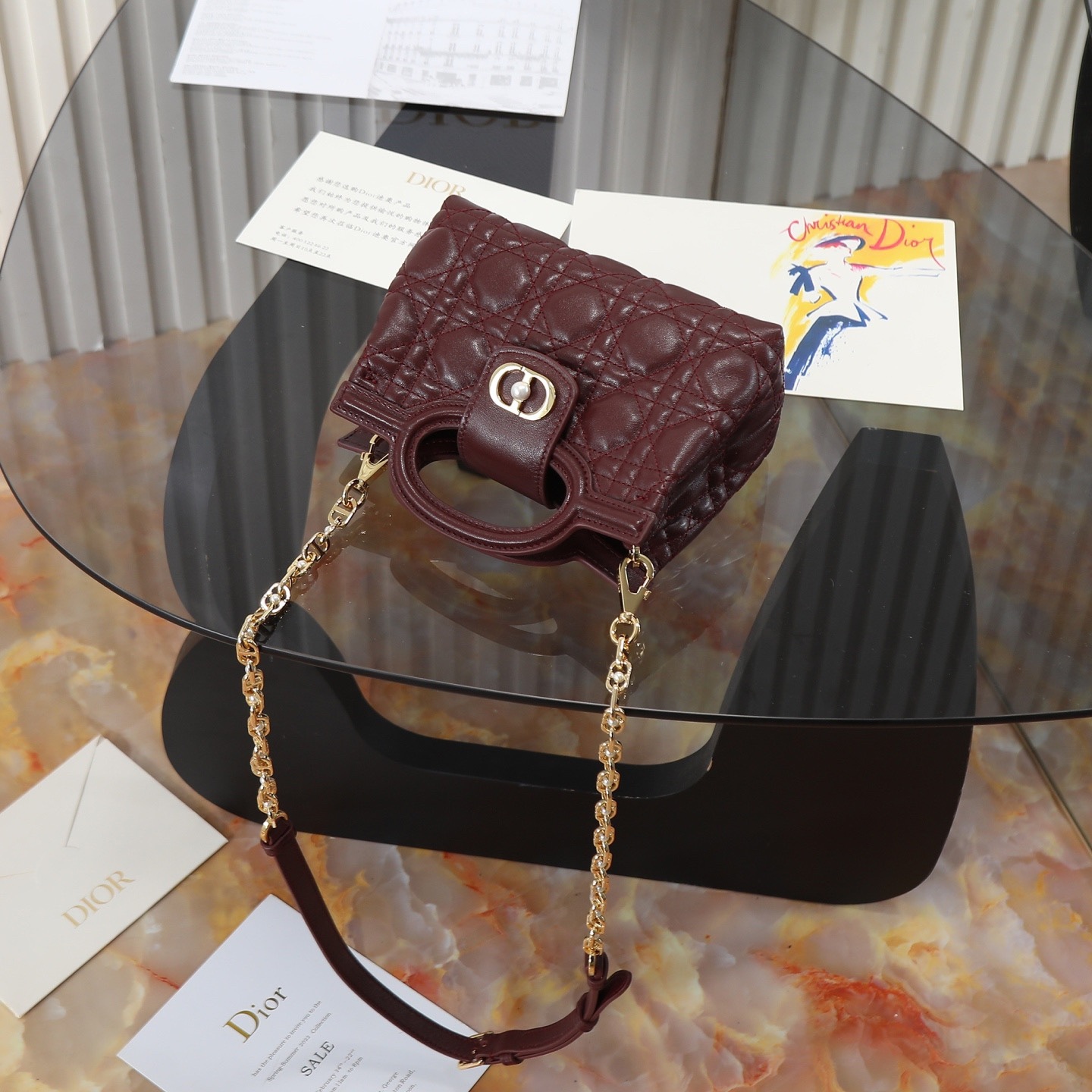 原廠級 酒紅色鏈條手袋
這款 Dior Jolie Top Handle 迷你鏈條手袋是二零二六早春成衣系列新品，呈現出優雅精緻的設計。採用黑色羊皮革精心製作，飾以藤格紋，翻蓋點綴以金色飾面金屬 CD 標誌和白色樹脂珠飾。內設一個隔層，可收納各種日常用品。搭配雙頂部手柄和可調節、可拆卸 CD 鏈條肩帶，肩帶由皮革帶和 CD 鏈環組成，飾以白色樹脂珠飾，可舒適手提、肩背或斜挎，可與日常或晚裝造型搭配。
