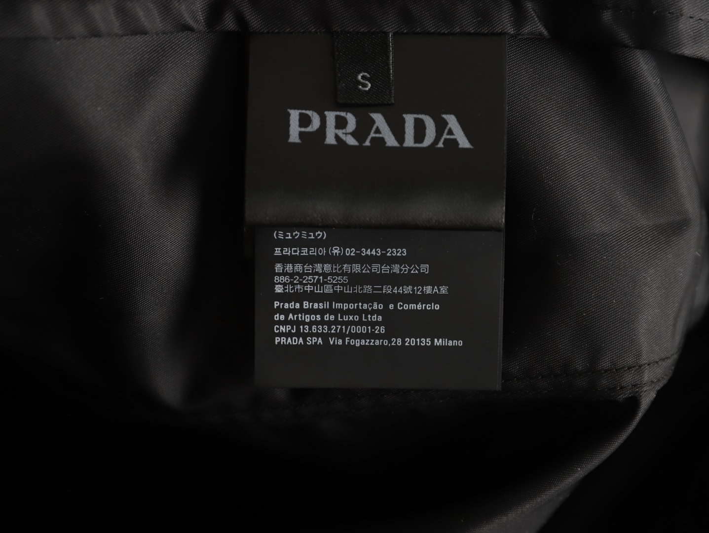 🔝PRADA/普拉達PRD 拉鍊口袋尼龍連帽外套
選用品牌標誌性的再生尼龍面料，與傳統尼龍性能相當，具備高強度，抗撕裂，耐磨損等特性。其質地輕盈，同時又具備防水功能適合多場景需求。抗皺，快乾的特點也易於日常打理維護。
定制三角徽標通過4個0.8mm金屬爪釘固定於衣身，爪釘背面經手工打磨至圓潤，避免刮蹭。下擺彈力抽繩選用7芯高彈尼龍繩，直徑3mm，配合橡膠扣，可實現±5cm長度調節。抽繩孔採用「金屬雞眼+防磨環」雙重保護，雞眼內徑5mm，邊緣光滑無毛刺，反復抽拉500次無變形。
袖口採用紐扣調