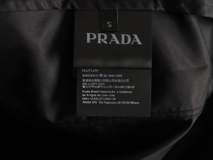 🔝PRADA/普拉達PRD 拉鍊口袋尼龍連帽外套
選用品牌標誌性的再生尼龍面料，與傳統尼龍性能相當，具備高強度，抗撕裂，耐磨損等特性。其質地輕盈，同時又具備防水功能適合多場景需求。抗皺，快乾的特點也易於日常打理維護。
定制三角徽標通過4個0.8mm金屬爪釘固定於衣身，爪釘背面經手工打磨至圓潤，避免刮蹭。下擺彈力抽繩選用7芯高彈尼龍繩，直徑3mm，配合橡膠扣，可實現±5cm長度調節。抽繩孔採用「金屬雞眼+防磨環」雙重保護，雞眼內徑5mm，邊緣光滑無毛刺，反復抽拉500次無變形。
袖口採用紐扣調