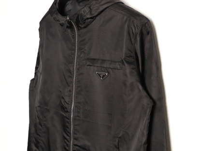 🔝PRADA/普拉達PRD 拉鍊口袋尼龍連帽外套
選用品牌標誌性的再生尼龍面料，與傳統尼龍性能相當，具備高強度，抗撕裂，耐磨損等特性。其質地輕盈，同時又具備防水功能適合多場景需求。抗皺，快乾的特點也易於日常打理維護。
定制三角徽標通過4個0.8mm金屬爪釘固定於衣身，爪釘背面經手工打磨至圓潤，避免刮蹭。下擺彈力抽繩選用7芯高彈尼龍繩，直徑3mm，配合橡膠扣，可實現±5cm長度調節。抽繩孔採用「金屬雞眼+防磨環」雙重保護，雞眼內徑5mm，邊緣光滑無毛刺，反復抽拉500次無變形。
袖口採用紐扣調