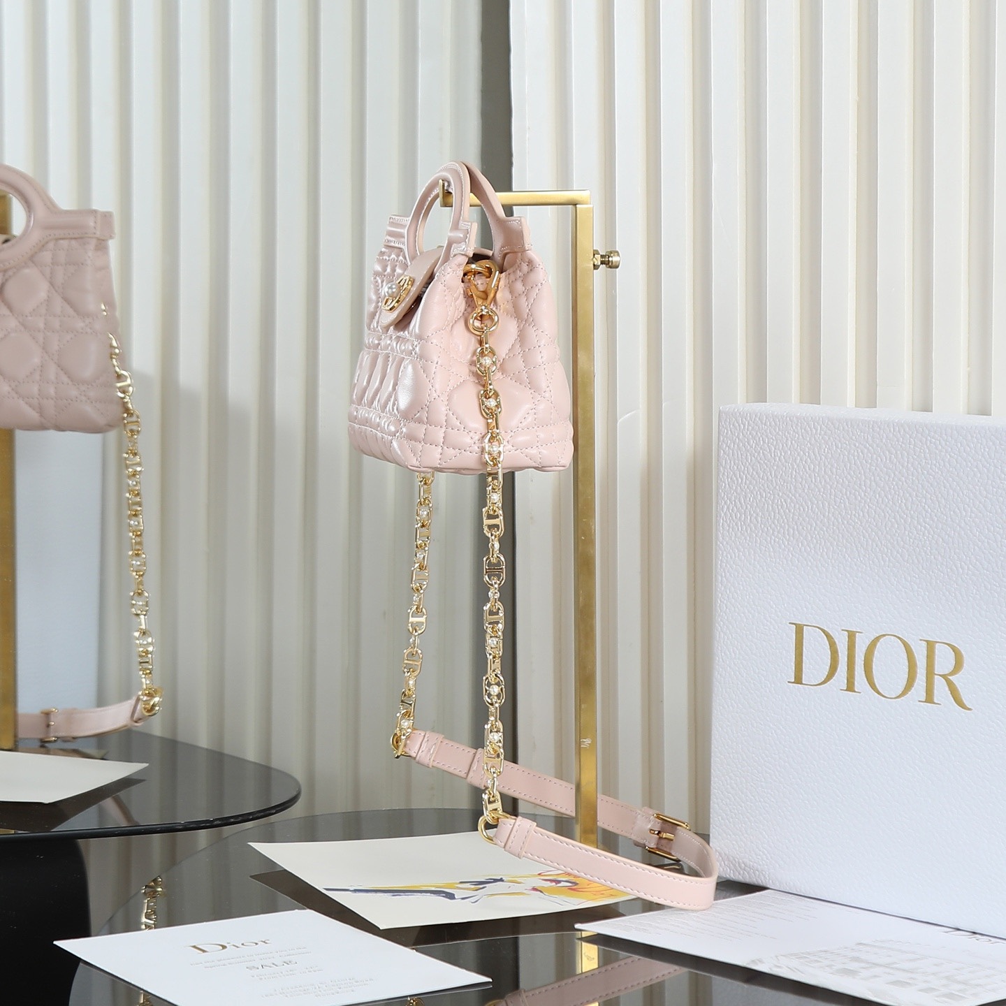 原廠級 粉色鏈條手袋
這款 Dior Jolie Top Handle 迷你鏈條手袋是二零二六早春成衣系列新品，呈現出優雅精緻的設計。採用黑色羊皮革精心製作，飾以藤格紋，翻蓋點綴以金色飾面金屬 CD 標誌和白色樹脂珠飾。內設一個隔層，可收納各種日常用品。搭配雙頂部手柄和可調節、可拆卸 CD 鏈條肩帶，肩帶由皮革帶和 CD 鏈環組成，飾以白色樹脂珠飾，可舒適手提、肩背或斜挎，可與日常或晚裝造型搭配。
