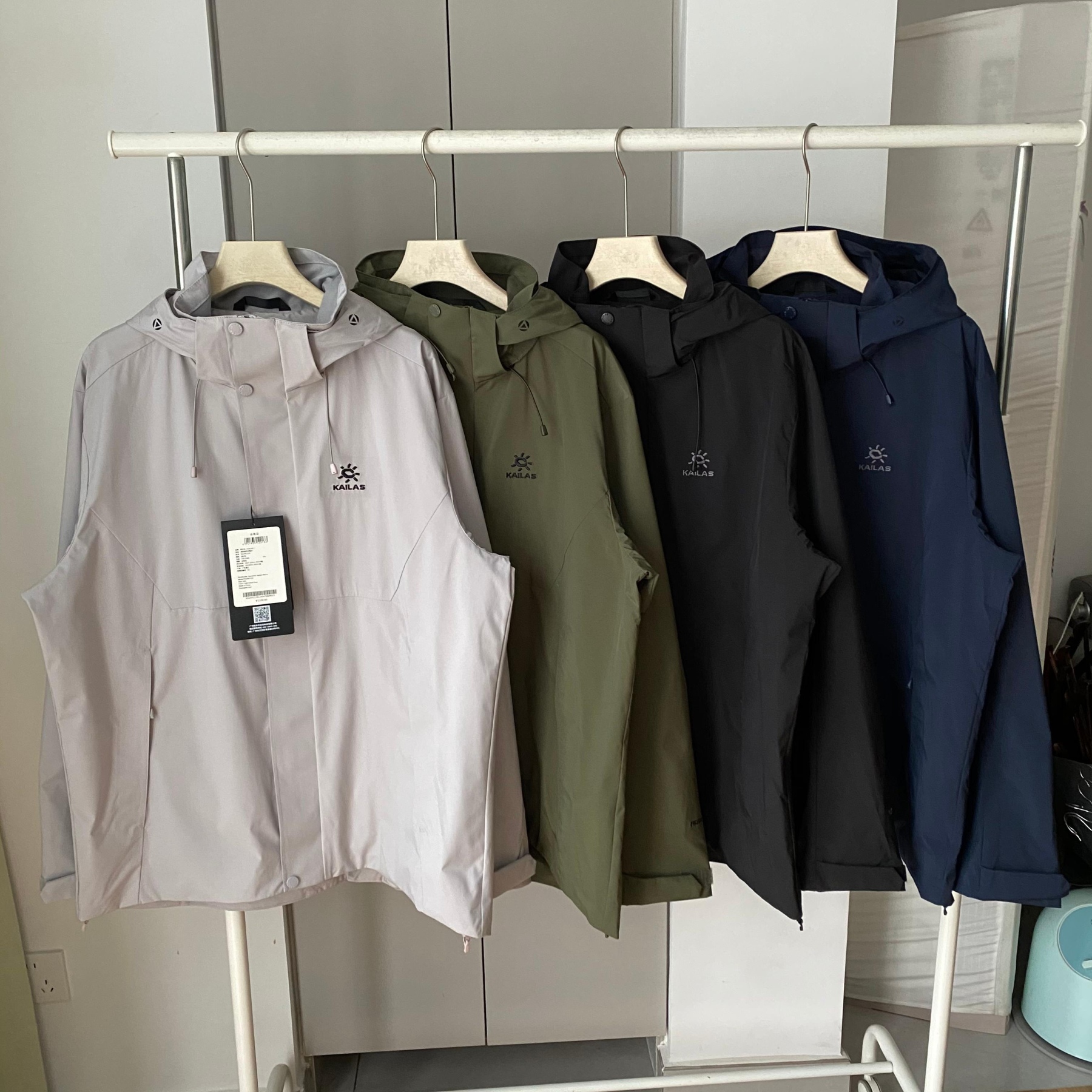 新款連帽三色風衣凱樂石KALIAS春季男子速乾輕薄外套 它的連帽設計，不僅時尚，還能在多變天氣中為你遮風擋雨。精選優質面料，觸感舒適，穿著自在無束縛，且具備良好的透氣性與耐磨性，滿足你的各種活動需求。版型上，注重亞洲人體型特點，舒適百搭，可輕鬆搭配各類下裝。無論是搭配牛仔褲展現休閒風，還是搭配工裝褲凸顯硬朗氣質，都毫無壓力。細節之處盡顯品質，精緻的縫線工藝，耐用的拉鍊與扣件，每一處都經過精心考量，只為給你帶來極致的穿著體驗。真正的3D立體裁剪，袖口添加魔術貼可自由調節 真正做到貼合身材比例，