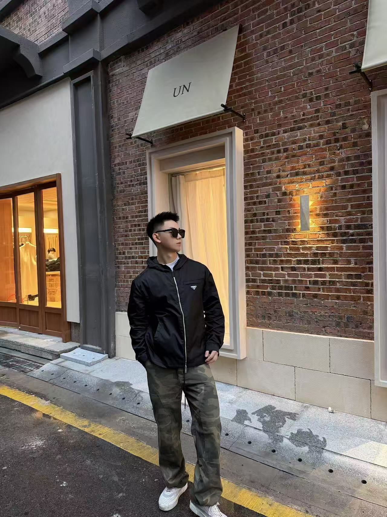 🔝PRADA/普拉達PRD 拉鍊口袋尼龍連帽外套
選用品牌標誌性的再生尼龍面料，與傳統尼龍性能相當，具備高強度，抗撕裂，耐磨損等特性。其質地輕盈，同時又具備防水功能適合多場景需求。抗皺，快乾的特點也易於日常打理維護。
定制三角徽標通過4個0.8mm金屬爪釘固定於衣身，爪釘背面經手工打磨至圓潤，避免刮蹭。下擺彈力抽繩選用7芯高彈尼龍繩，直徑3mm，配合橡膠扣，可實現±5cm長度調節。抽繩孔採用「金屬雞眼+防磨環」雙重保護，雞眼內徑5mm，邊緣光滑無毛刺，反復抽拉500次無變形。
袖口採用紐扣調