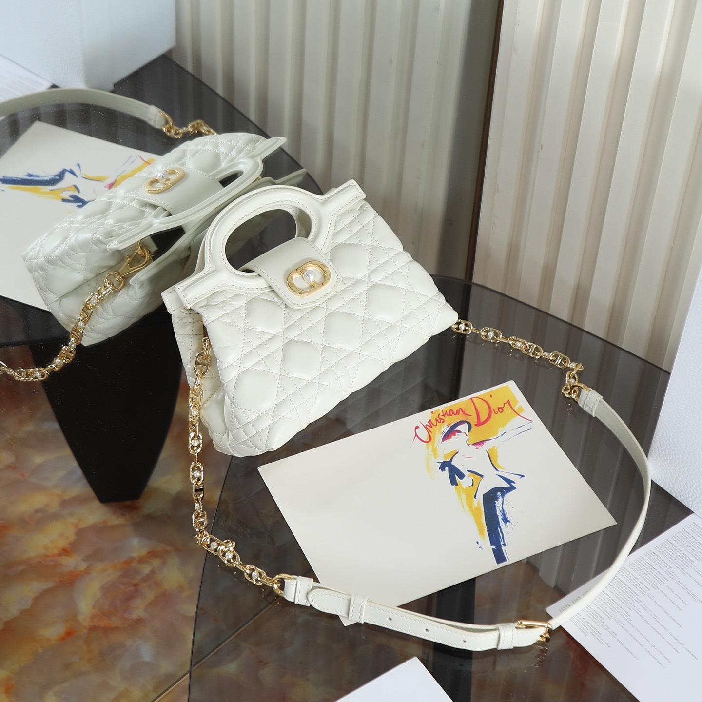 原廠級 白色鏈條手袋
這款 Dior Jolie Top Handle 迷你鏈條手袋是二零二六早春成衣系列新品，呈現出優雅精緻的設計。採用黑色羊皮革精心製作，飾以藤格紋，翻蓋點綴以金色飾面金屬 CD 標誌和白色樹脂珠飾。內設一個隔層，可收納各種日常用品。搭配雙頂部手柄和可調節、可拆卸 CD 鏈條肩帶，肩帶由皮革帶和 CD 鏈環組成，飾以白色樹脂珠飾，可舒適手提、肩背或斜挎，可與日常或晚裝造型搭配。
