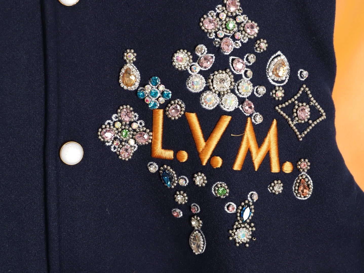 Louis Vuitton/路易威登 26ss 水鑽刺繡棒球服外套
材質拼接：衣身採用藏青色羊毛混紡面料，質感挺括耐磨；袖子為淺棕牛皮材質，柔軟細膩，經典拼皮設計還原美式棒球服復古感。

• 裝飾亮點：左胸位置有重工水鑽+金屬刺繡裝飾，鑲嵌多色寶石與閃鑽，綴有“L.V.M.”字母標識，華麗精緻，辨識度拉滿。

• 版型結構：立領+羅紋條紋領口/袖口/下擺，防風且修飾身形；正面按扣開合，兩側配有插袋，兼顧實用與美觀。
球帽點綴，休閒隨性又有街頭感。
N Size:S-XL