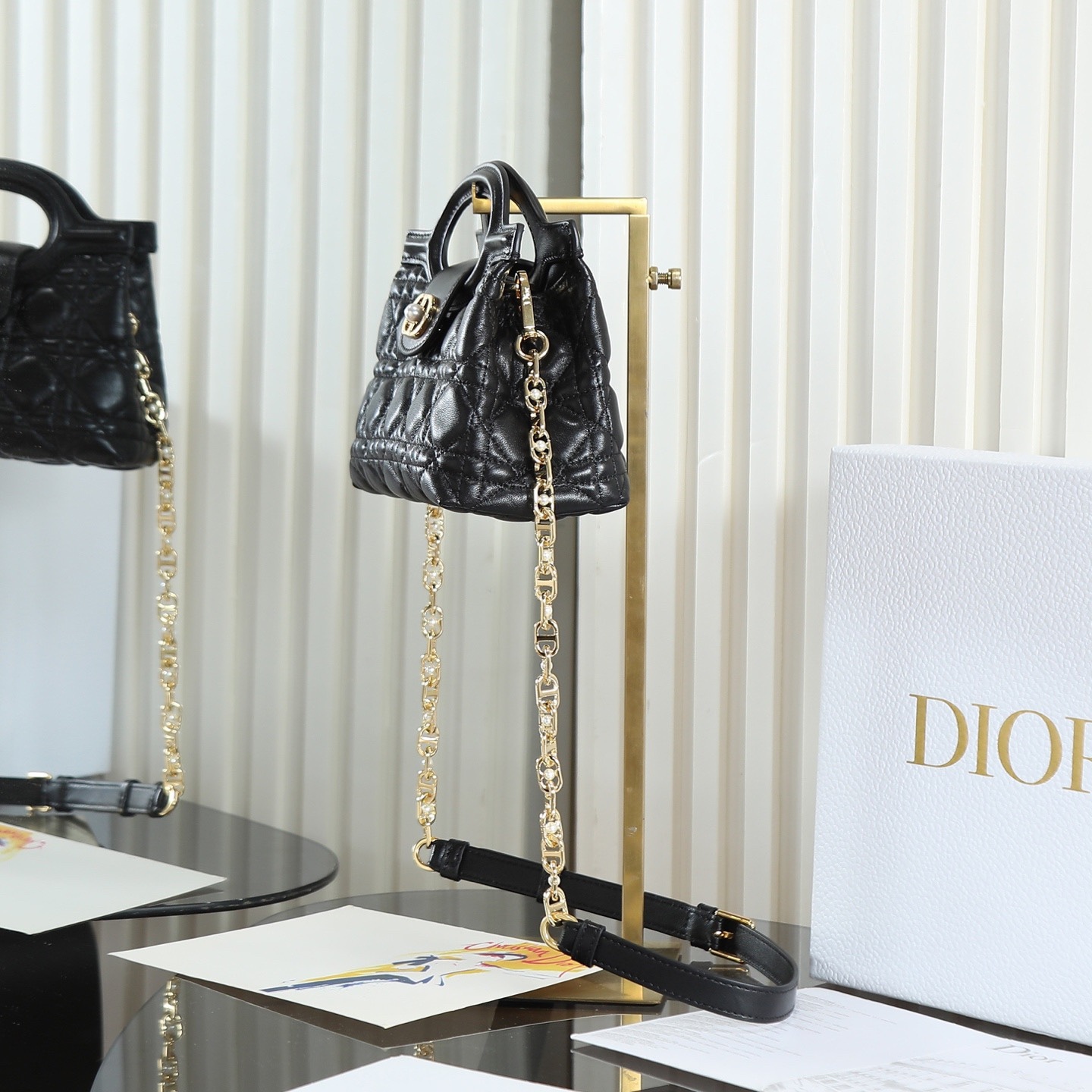 原廠級 黑色鏈條手袋
這款 Dior Jolie Top Handle 迷你鏈條手袋是二零二六早春成衣系列新品，呈現出優雅精緻的設計。採用黑色羊皮革精心製作，飾以藤格紋，翻蓋點綴以金色飾面金屬 CD 標誌和白色樹脂珠飾。內設一個隔層，可收納各種日常用品。搭配雙頂部手柄和可調節、可拆卸 CD 鏈條肩帶，肩帶由皮革帶和 CD 鏈環組成，飾以白色樹脂珠飾，可舒適手提、肩背或斜挎，可與日常或晚裝造型搭配。
