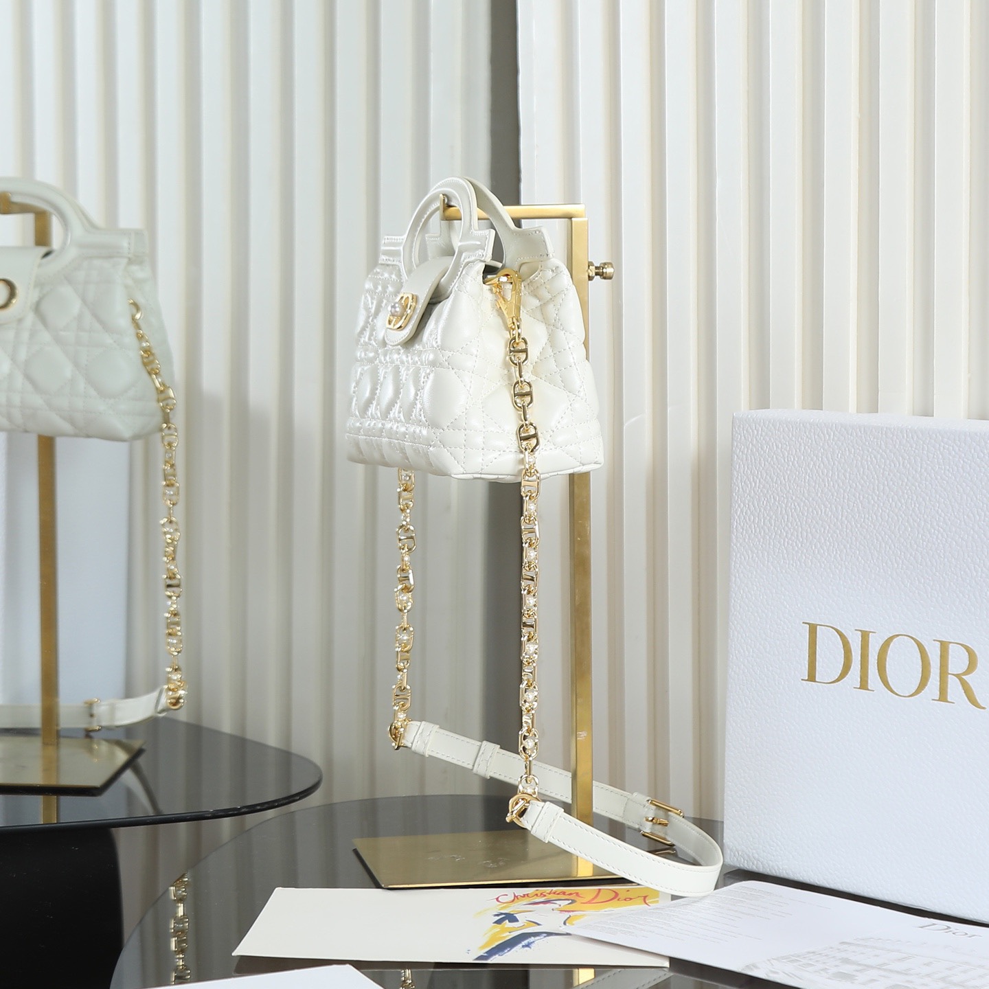 原廠級 白色鏈條手袋
這款 Dior Jolie Top Handle 迷你鏈條手袋是二零二六早春成衣系列新品，呈現出優雅精緻的設計。採用黑色羊皮革精心製作，飾以藤格紋，翻蓋點綴以金色飾面金屬 CD 標誌和白色樹脂珠飾。內設一個隔層，可收納各種日常用品。搭配雙頂部手柄和可調節、可拆卸 CD 鏈條肩帶，肩帶由皮革帶和 CD 鏈環組成，飾以白色樹脂珠飾，可舒適手提、肩背或斜挎，可與日常或晚裝造型搭配。
