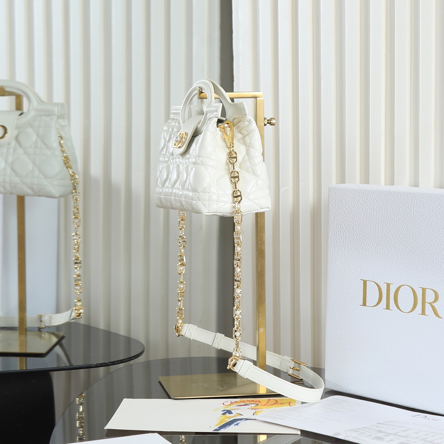 原廠級 白色鏈條手袋
這款 Dior Jolie Top Handle 迷你鏈條手袋是二零二六早春成衣系列新品，呈現出優雅精緻的設計。採用黑色羊皮革精心製作，飾以藤格紋，翻蓋點綴以金色飾面金屬 CD 標誌和白色樹脂珠飾。內設一個隔層，可收納各種日常用品。搭配雙頂部手柄和可調節、可拆卸 CD 鏈條肩帶，肩帶由皮革帶和 CD 鏈環組成，飾以白色樹脂珠飾，可舒適手提、肩背或斜挎，可與日常或晚裝造型搭配。
