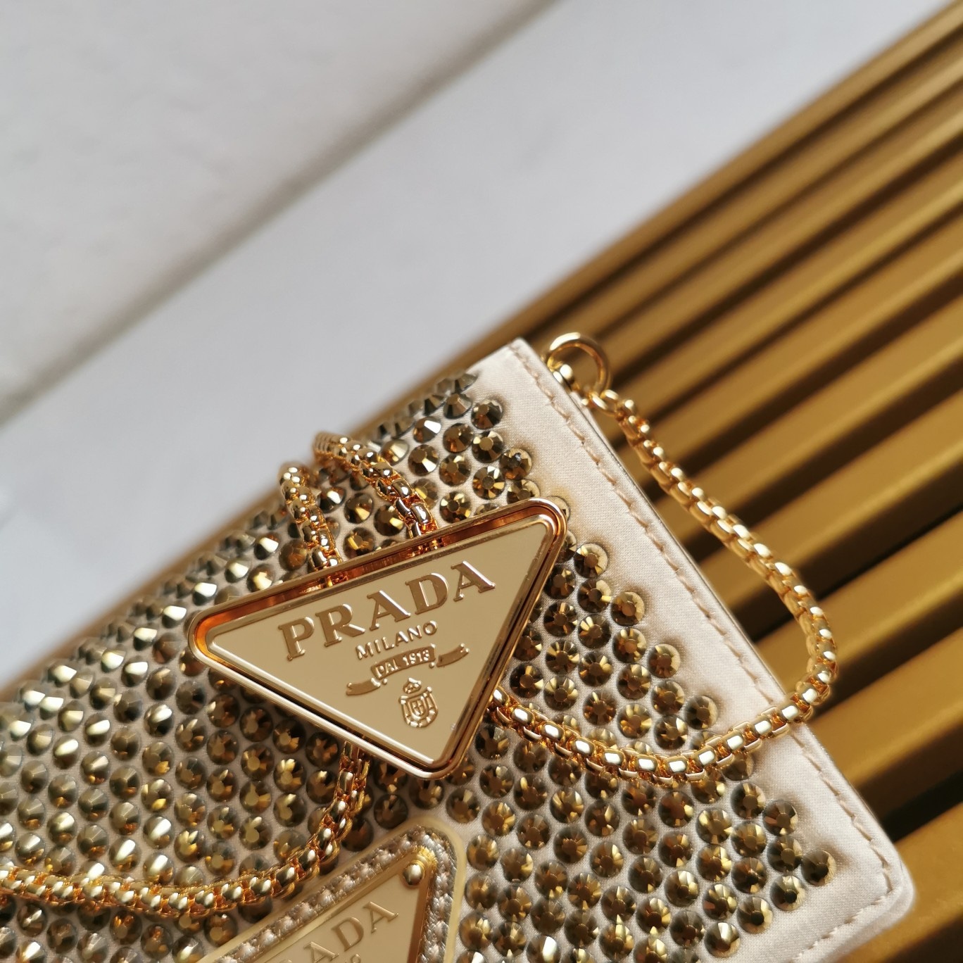 【 原單】🎉2023新款金色系項鍊水晶小包🎉1MR024🎉🎉這款Duchesse面料卡片夾通體飾以仿水晶，於表面營造出光影格調和虹彩炫色，彰顯華美且不失功能性的設計。最愛是這條可拆卸可調節鐵璉肩帶，又可當腰包裝飾😍😍又可當搭配衣服項鍊裝飾，中間三角形標可調節活動，賦予單品多樣的佩戴方式。空間可裝口紅💄/耳機/鑰匙🚗....夜燈下bling bling,太美了。值得入手🎉🎉尺寸：長11.5cm*高8cm