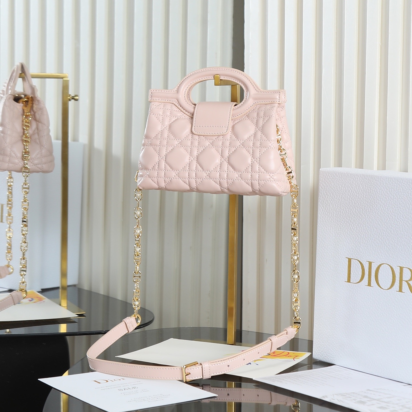 原廠級 粉色鏈條手袋
這款 Dior Jolie Top Handle 迷你鏈條手袋是二零二六早春成衣系列新品，呈現出優雅精緻的設計。採用黑色羊皮革精心製作，飾以藤格紋，翻蓋點綴以金色飾面金屬 CD 標誌和白色樹脂珠飾。內設一個隔層，可收納各種日常用品。搭配雙頂部手柄和可調節、可拆卸 CD 鏈條肩帶，肩帶由皮革帶和 CD 鏈環組成，飾以白色樹脂珠飾，可舒適手提、肩背或斜挎，可與日常或晚裝造型搭配。
