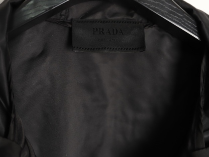 🔝PRADA/普拉達PRD 拉鍊口袋尼龍連帽外套
選用品牌標誌性的再生尼龍面料，與傳統尼龍性能相當，具備高強度，抗撕裂，耐磨損等特性。其質地輕盈，同時又具備防水功能適合多場景需求。抗皺，快乾的特點也易於日常打理維護。
定制三角徽標通過4個0.8mm金屬爪釘固定於衣身，爪釘背面經手工打磨至圓潤，避免刮蹭。下擺彈力抽繩選用7芯高彈尼龍繩，直徑3mm，配合橡膠扣，可實現±5cm長度調節。抽繩孔採用「金屬雞眼+防磨環」雙重保護，雞眼內徑5mm，邊緣光滑無毛刺，反復抽拉500次無變形。
袖口採用紐扣調