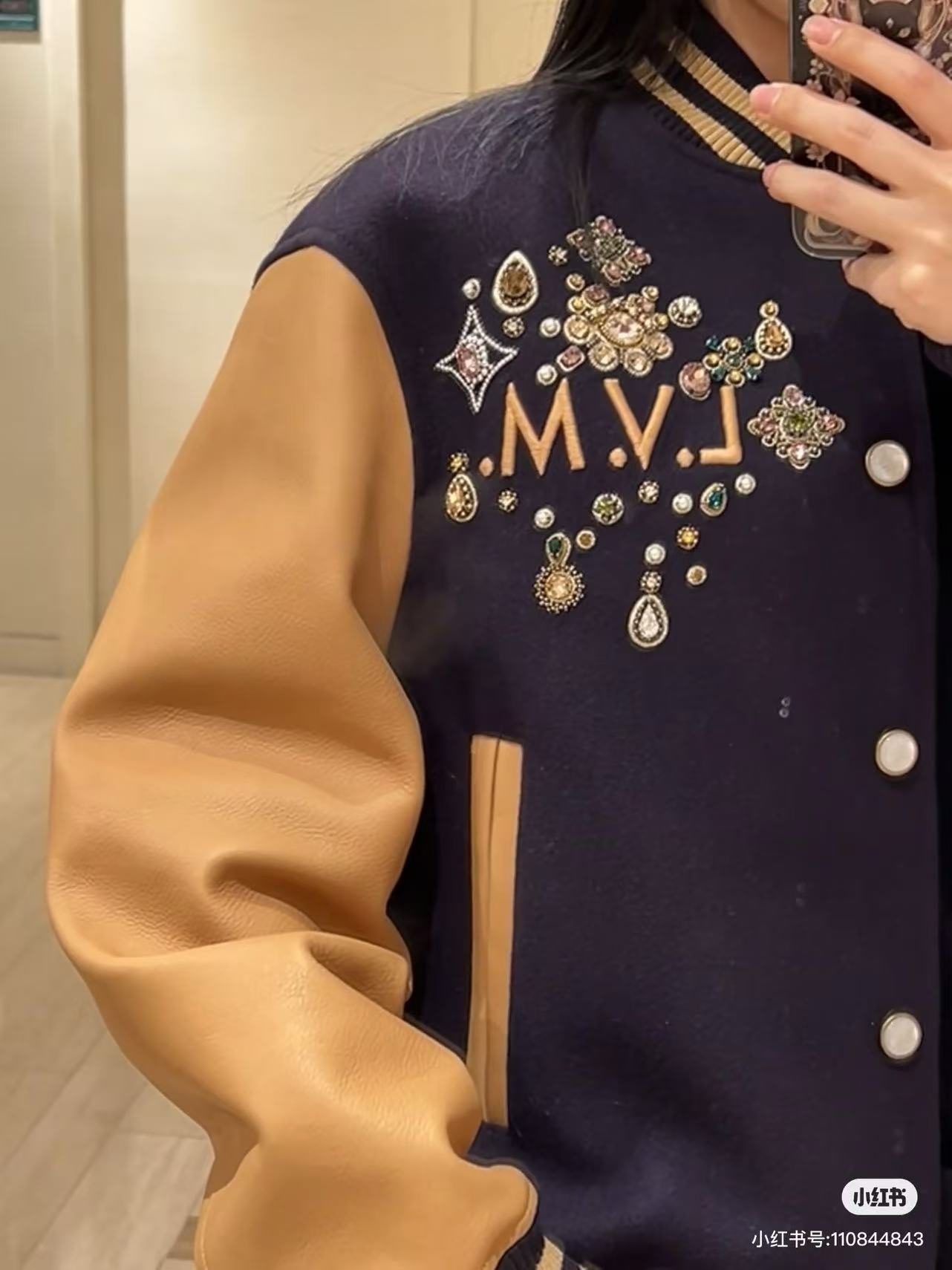 Louis Vuitton/路易威登 26ss 水鑽刺繡棒球服外套
材質拼接：衣身採用藏青色羊毛混紡面料，質感挺括耐磨；袖子為淺棕牛皮材質，柔軟細膩，經典拼皮設計還原美式棒球服復古感。

• 裝飾亮點：左胸位置有重工水鑽+金屬刺繡裝飾，鑲嵌多色寶石與閃鑽，綴有“L.V.M.”字母標識，華麗精緻，辨識度拉滿。

• 版型結構：立領+羅紋條紋領口/袖口/下擺，防風且修飾身形；正面按扣開合，兩側配有插袋，兼顧實用與美觀。
球帽點綴，休閒隨性又有街頭感。
N Size:S-XL