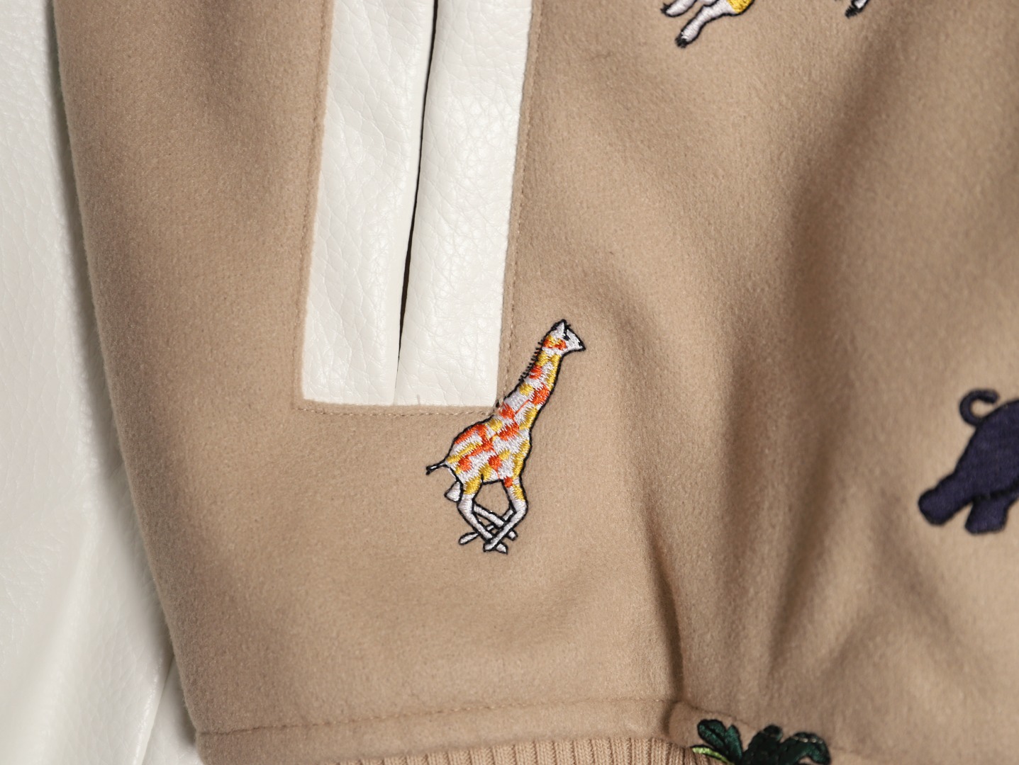 Louis Vuitton/路易威登 26ss 動物樂園刺繡棒球服外套
材質拼接：衣身採用淺卡其色羊毛混紡面料，柔軟且有挺括感；袖子為奶白色荔枝紋牛皮，質感細膩，淺色系搭配更顯清爽。

• 裝飾亮點：衣身滿印精緻動物刺繡（長頸鹿、斑馬、大象、黑豹等）與棕櫚樹圖案，左胸綴有“L.V.M.”字母標識，充滿童趣與度假感，辨識度極高。

• 版型結構：經典棒球服版型，羅紋條紋領口/袖口/下擺，防風收型；正面按扣開合，兩側配白色撞色插袋，兼顧實用性與設計感。
N SIZE:S-XL
