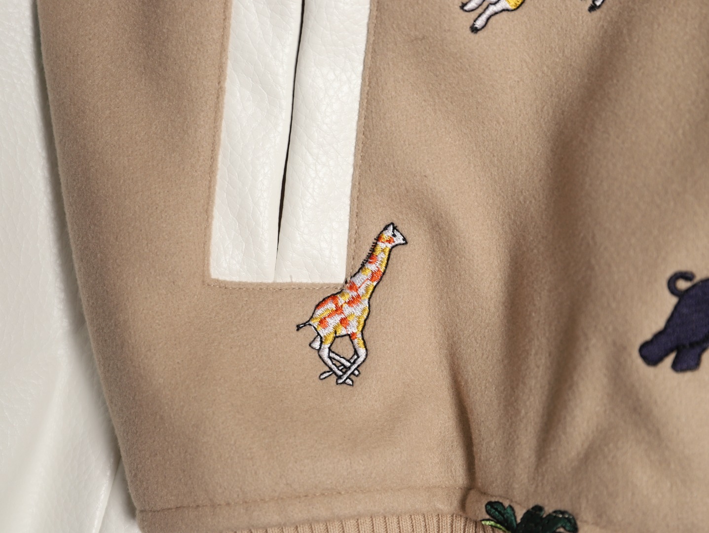 Louis Vuitton/路易威登 26ss 動物樂園刺繡棒球服外套
材質拼接：衣身採用淺卡其色羊毛混紡面料，柔軟且有挺括感；袖子為奶白色荔枝紋牛皮，質感細膩，淺色系搭配更顯清爽。

• 裝飾亮點：衣身滿印精緻動物刺繡（長頸鹿、斑馬、大象、黑豹等）與棕櫚樹圖案，左胸綴有“L.V.M.”字母標識，充滿童趣與度假感，辨識度極高。

• 版型結構：經典棒球服版型，羅紋條紋領口/袖口/下擺，防風收型；正面按扣開合，兩側配白色撞色插袋，兼顧實用性與設計感。
N SIZE:S-XL
