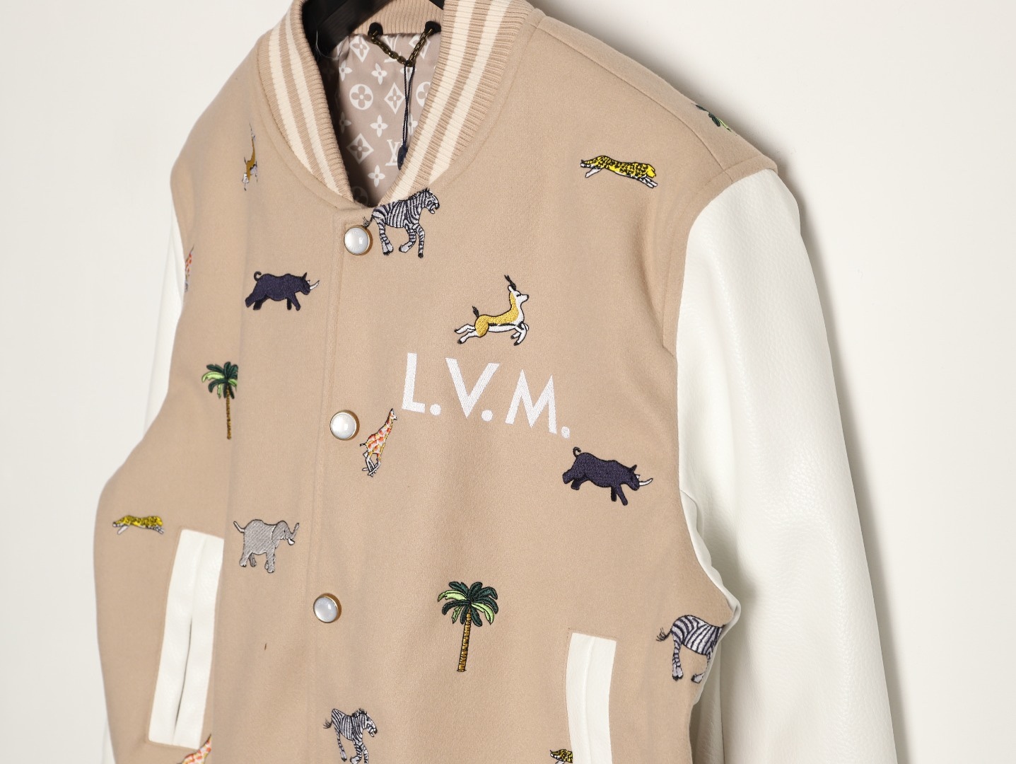 Louis Vuitton/路易威登 26ss 動物樂園刺繡棒球服外套
材質拼接：衣身採用淺卡其色羊毛混紡面料，柔軟且有挺括感；袖子為奶白色荔枝紋牛皮，質感細膩，淺色系搭配更顯清爽。

• 裝飾亮點：衣身滿印精緻動物刺繡（長頸鹿、斑馬、大象、黑豹等）與棕櫚樹圖案，左胸綴有“L.V.M.”字母標識，充滿童趣與度假感，辨識度極高。

• 版型結構：經典棒球服版型，羅紋條紋領口/袖口/下擺，防風收型；正面按扣開合，兩側配白色撞色插袋，兼顧實用性與設計感。
N SIZE:S-XL
