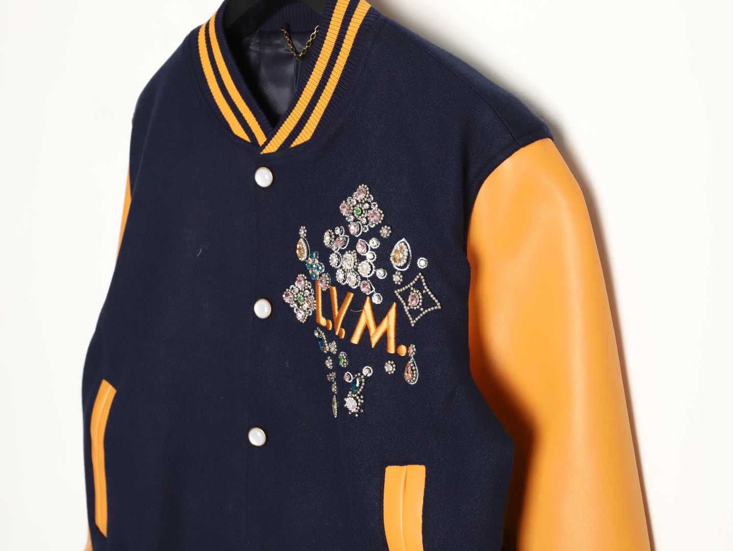Louis Vuitton/路易威登 26ss 水鑽刺繡棒球服外套
材質拼接：衣身採用藏青色羊毛混紡面料，質感挺括耐磨；袖子為淺棕牛皮材質，柔軟細膩，經典拼皮設計還原美式棒球服復古感。

• 裝飾亮點：左胸位置有重工水鑽+金屬刺繡裝飾，鑲嵌多色寶石與閃鑽，綴有“L.V.M.”字母標識，華麗精緻，辨識度拉滿。

• 版型結構：立領+羅紋條紋領口/袖口/下擺，防風且修飾身形；正面按扣開合，兩側配有插袋，兼顧實用與美觀。
球帽點綴，休閒隨性又有街頭感。
N Size:S-XL