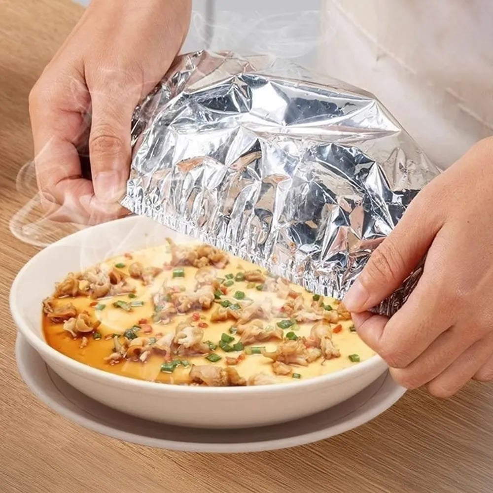 Hands lifting aluminum foil food cover from a serving bowl