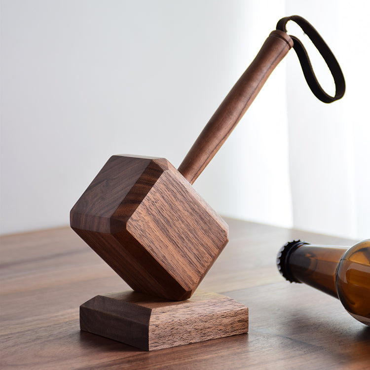 Wooden hammer-shape bottle opener with leather wrist strap on walnut counter beside blue-and-white ceramic bottle