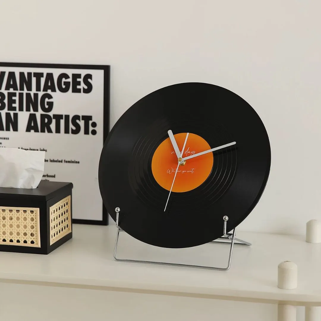 Black vinyl-record clock beside silver candle holder, wood frame, and open book