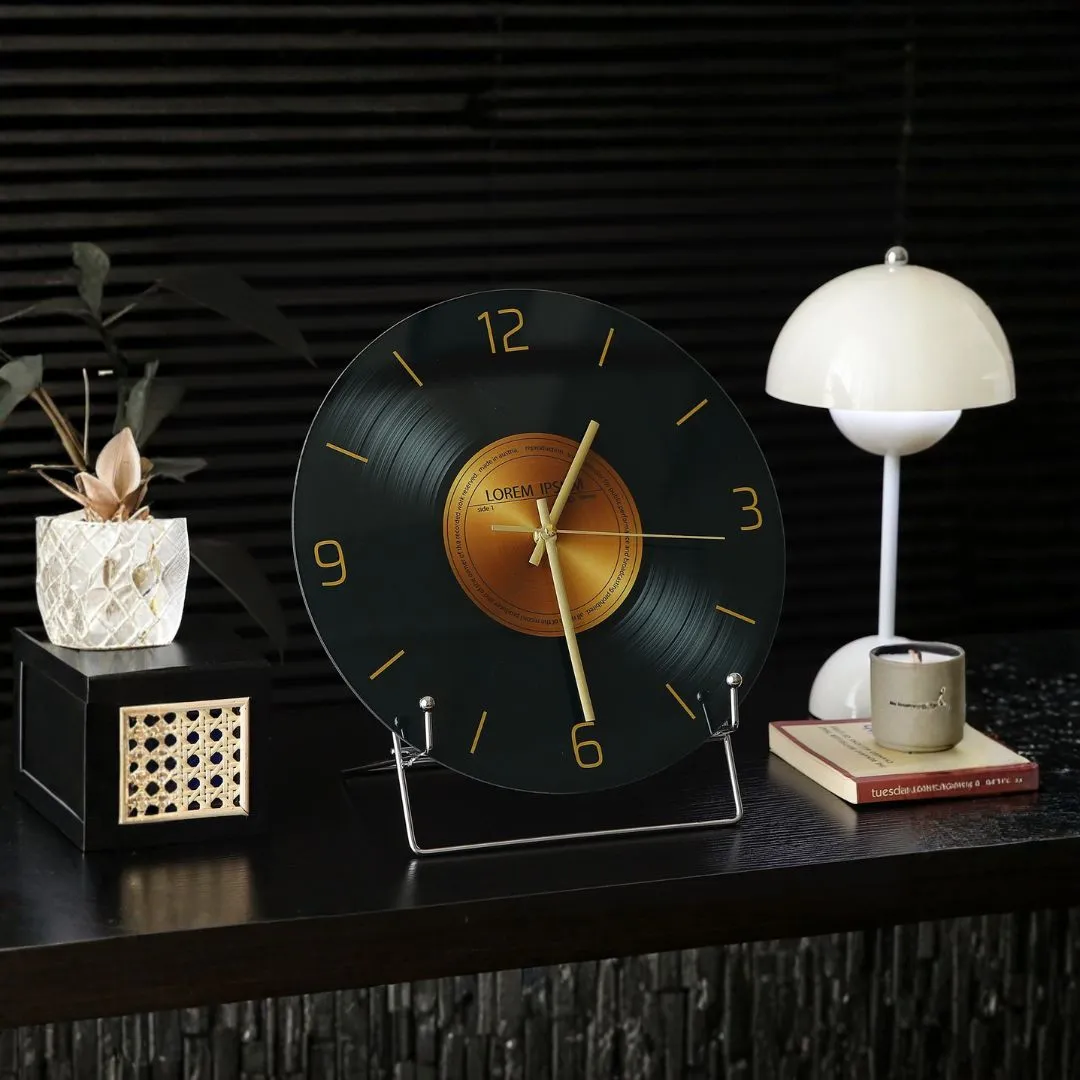 Vinyl-record clock with gold numerals on dark surface beside pleated lamp, candle and rattan box