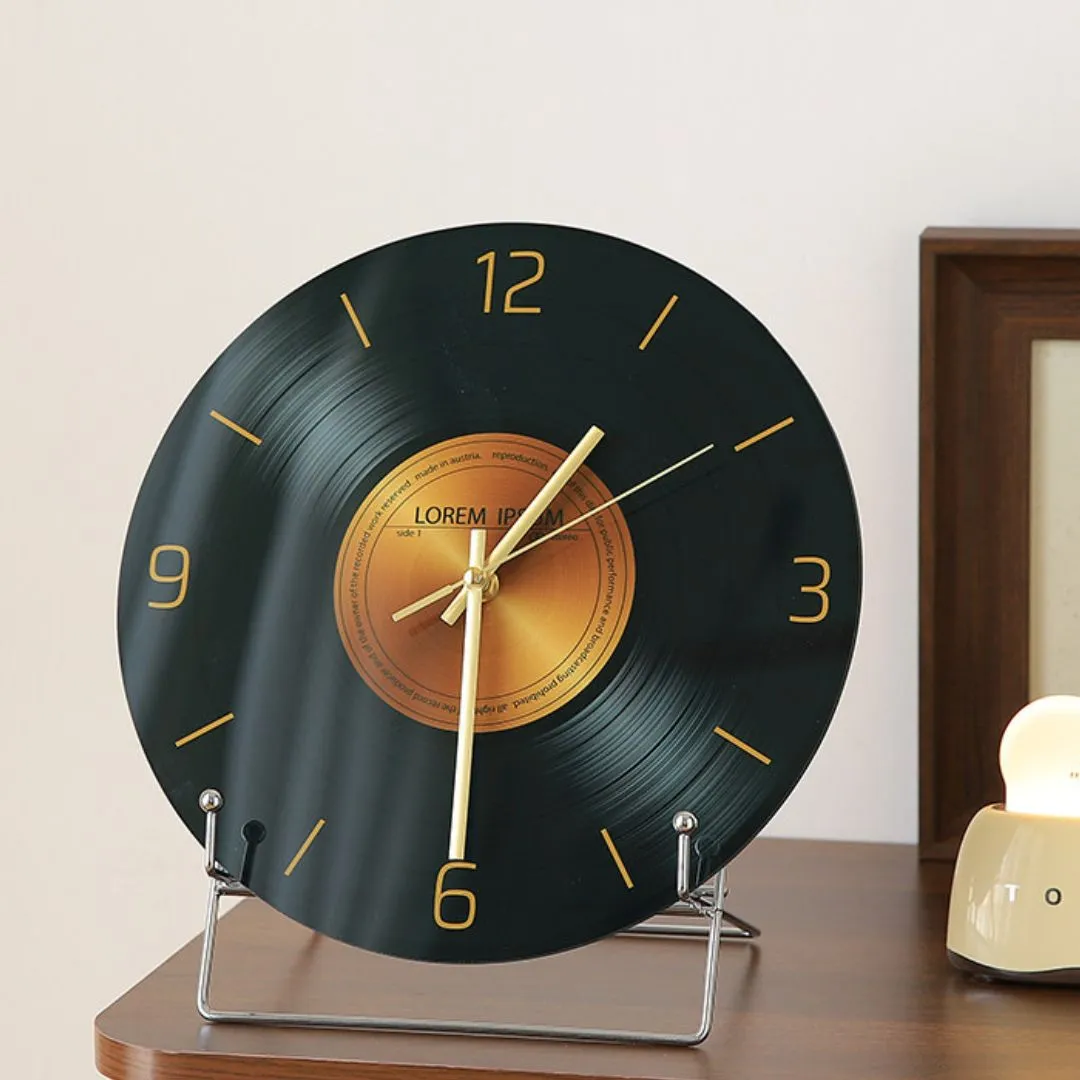 Tempered glass vinyl-record clock with gold LOREM IPSUM label on chrome stand beside wooden frame and cream lamp