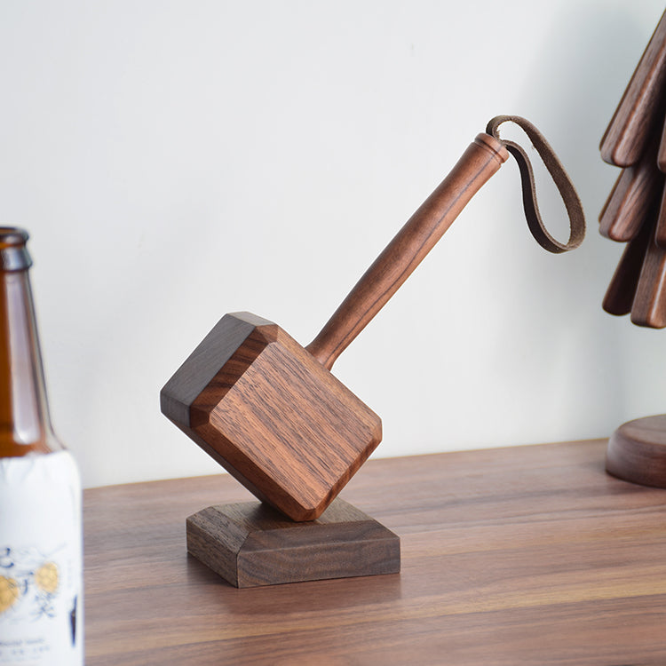 Wooden hammer bottle opener with leather wrist strap on dark wood counter beside green plant in white vase