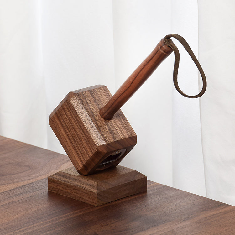 Walnut hammer bottle opener with leather wrist strap on counter beside capped amber beer bottle