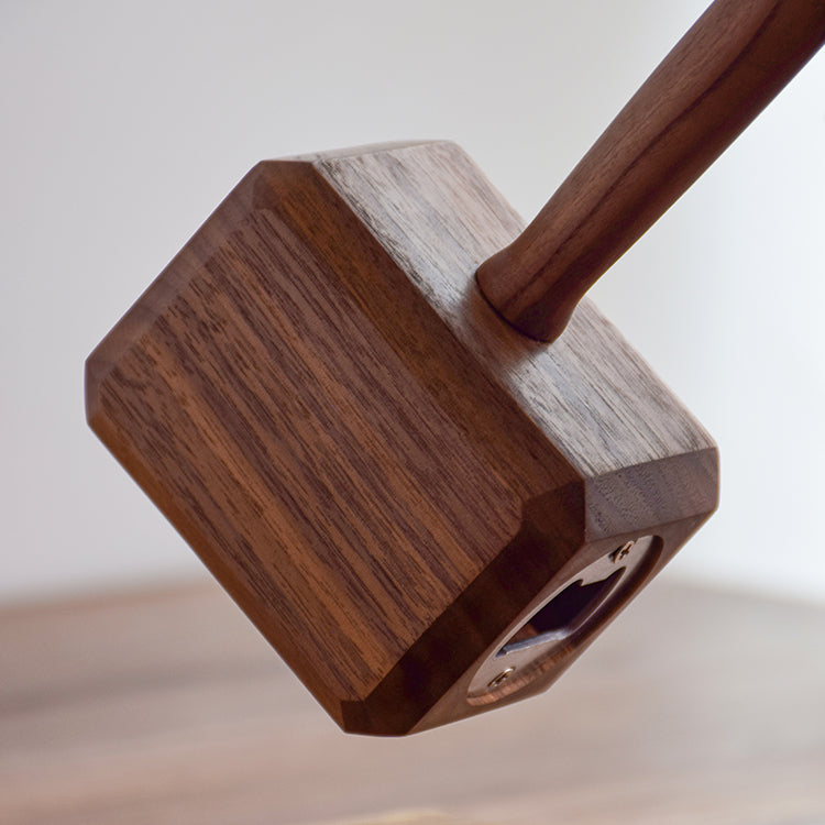 Walnut hammer bottle opener on its stand with leather wrist strap, white curtain background