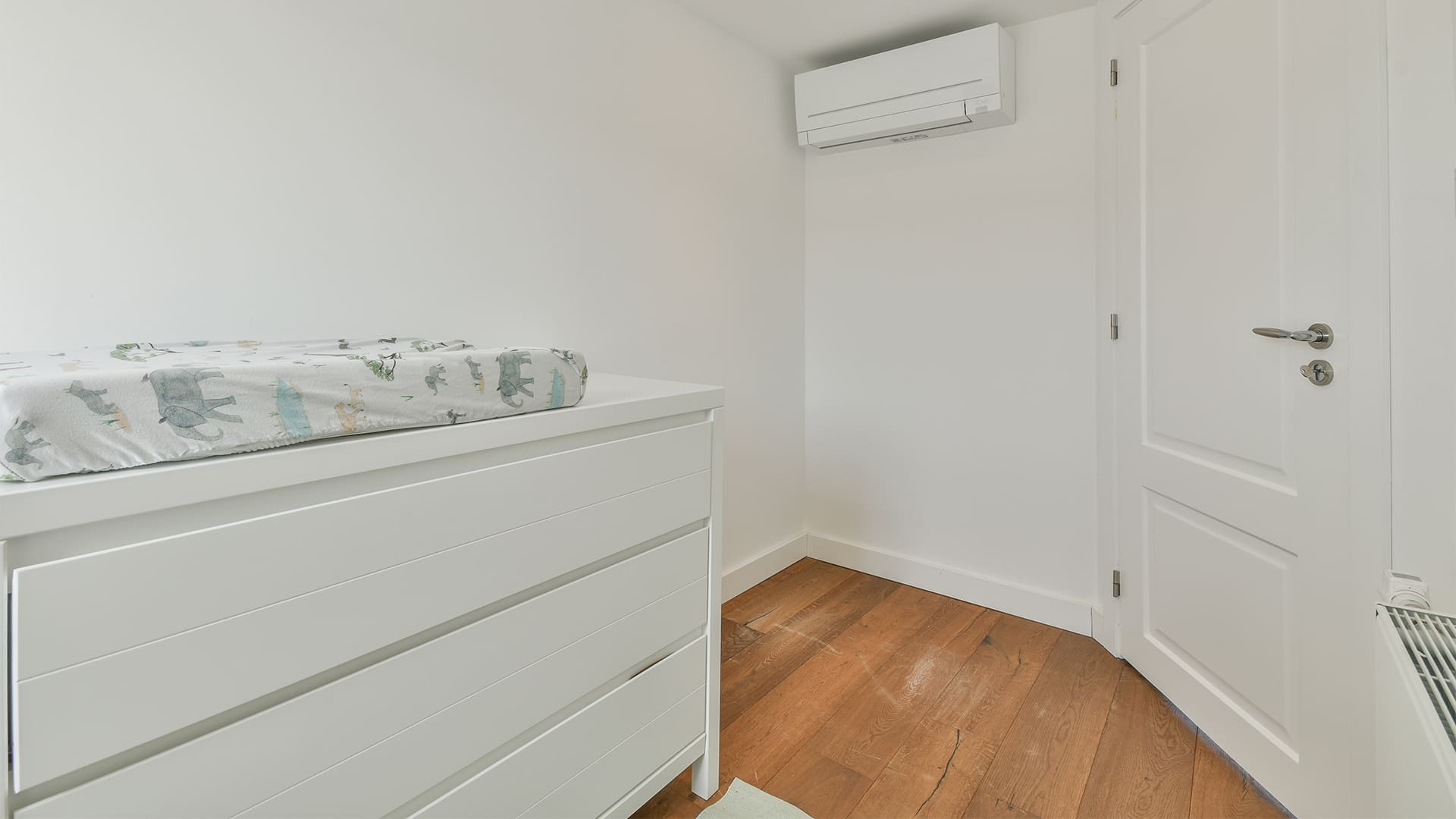 Minimalist white baby dresser with soft close drawers in a nursery corner
