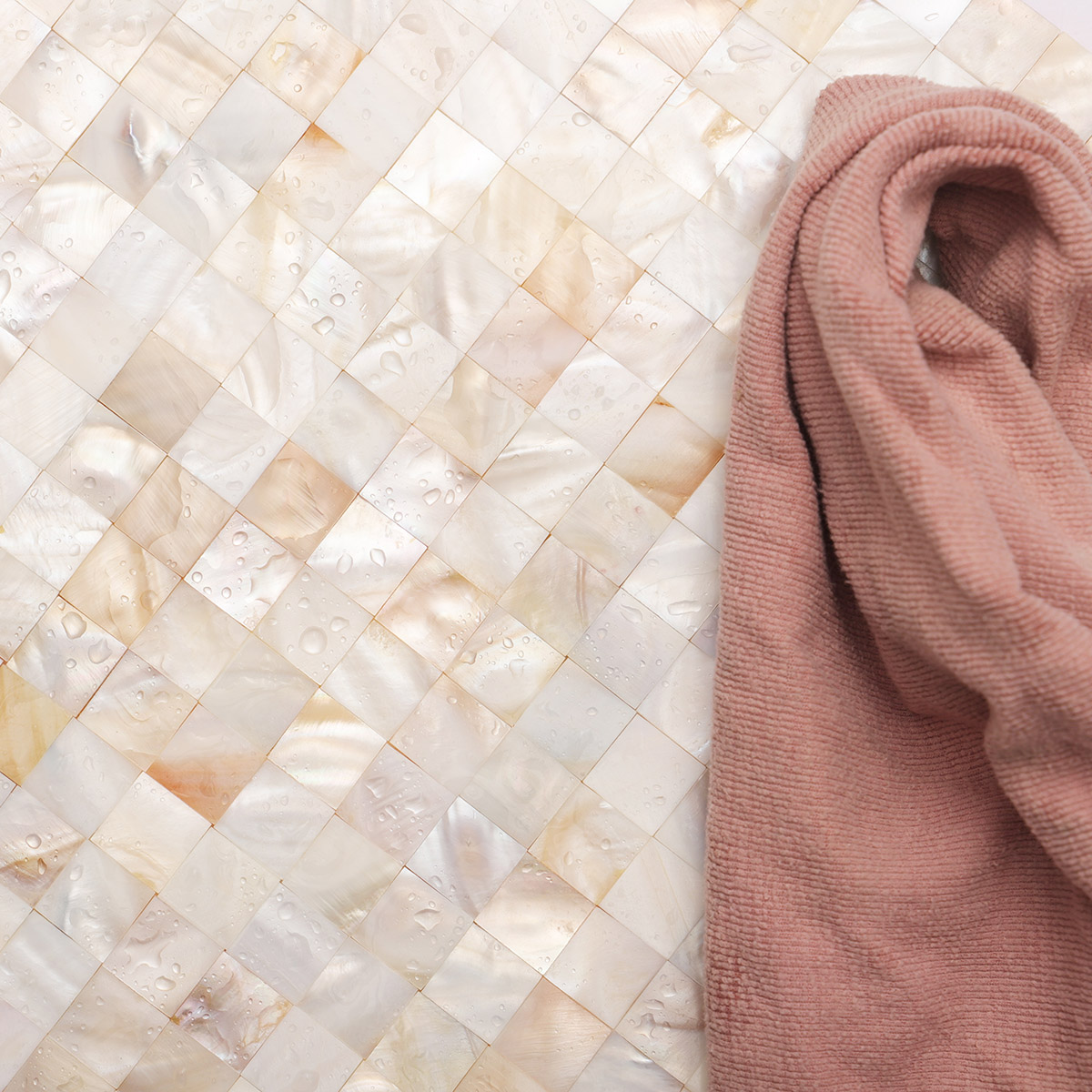 Natural mother of pearl mosaic tile with surface water and a towel.